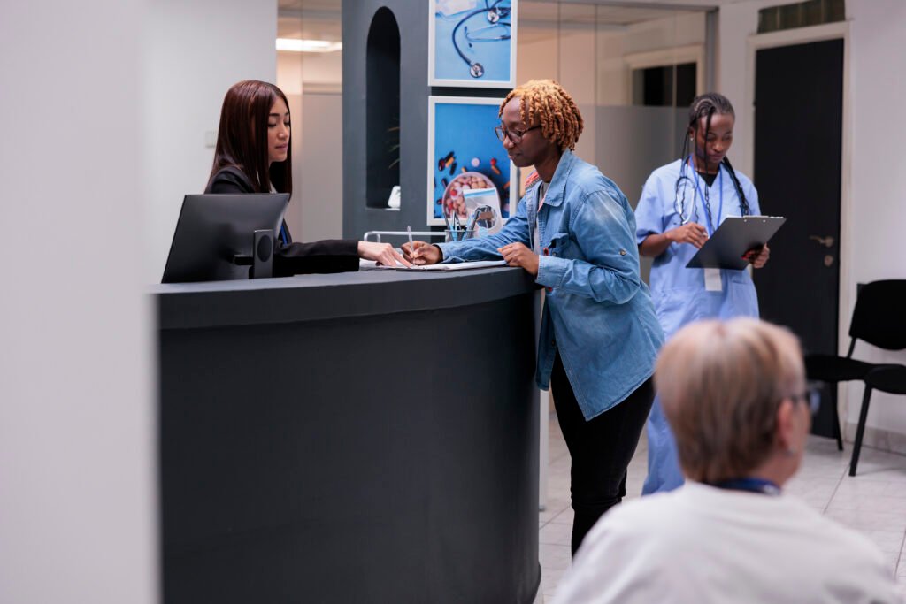 african american patient filling report papers talking receptionist hospital reception counter woman writing medical form before checkup appointment with doctor health center